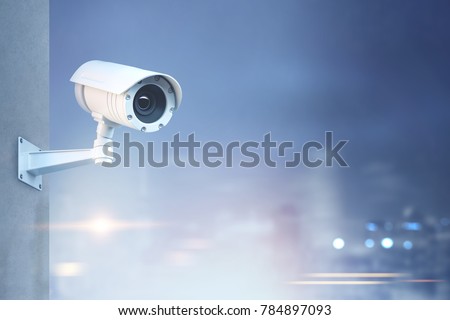Modern CCTV camera on a wall. A blurred night cityscape background. Concept of surveillance and monitoring. Toned image double exposure mock up