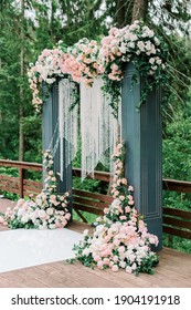 Modern ceremony in European style. Wedding arch with roses on the background of a forest lake and trees. Jewelry from natural flowers and crystals. Side view