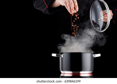 Modern chef in professional uniform adding spice to steaming pot