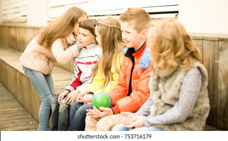 Modern Children On A Bench Playing Chinese Whispers