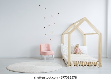 Modern Children's Furniture In A Spacious Bedroom With Star Stickers On The White Wall, And A Pastel Pink Comfortable Chic Chair Next To A Wooden Bed
