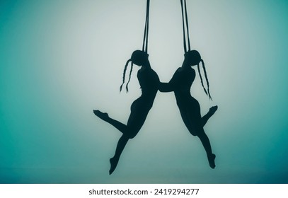 Modern choreography and acrobatics creative concept. Silhouette of two female acrobats on a blue neon background with a spotlight in the center. Female acrobats perform acrobatic elements on ropes.