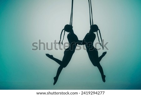 Modern choreography and acrobatics creative concept. Silhouette of two female acrobats on a blue neon background with a spotlight in the center. Female acrobats perform acrobatic elements on ropes.