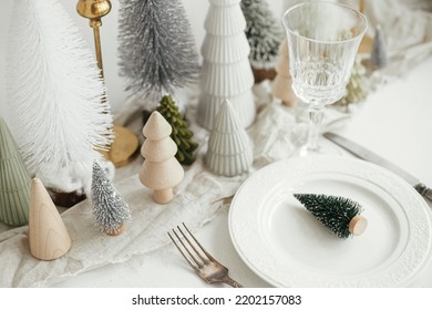 Modern Christmas Table Setting. Stylish Little Christmas Tree On Plate, Vintage Cutlery, Glasses, Festive Fir And Houses On White Rustic Table. Holiday Arrangement Of Table