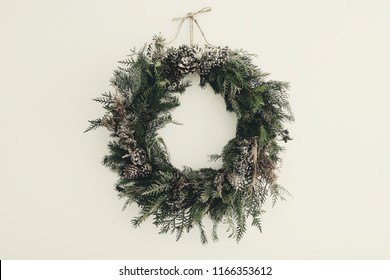 modern Christmas wreath. stylish rustic christmas wreath with pine cones,fir branches,snow, hanging on white wall. space for text. handmade decor for winter holidays