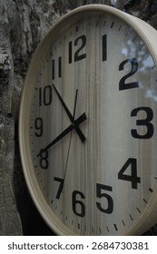 A modern, circular wall clock is shown in a close-up, angled view, resting against the rough, weathered texture of a tree stump or split log