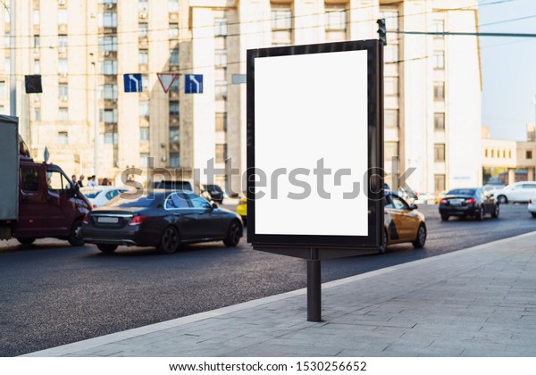 Modern city banner with blank screen standing\
by road. Busy traffic on urban highway. Trucks, cars passing by\
vertical billboard on city street. Multistoried office building,\
road signs in\
background.