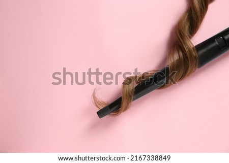 Modern clipless curling iron and brown hair lock on pink background, top view. Space for text