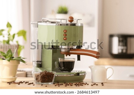 Modern coffee machine with cup and beans on table in kitchen
