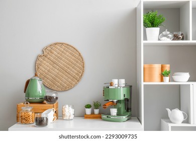 Modern coffee machine, cups, snacks and jar with coffee beans on table near white wall