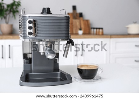 Modern coffee machine with glass cup of hot espresso on table in kitchen