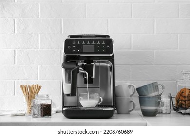 Máquina de café moderna vertiendo leche en taza de vidrio sobre la encimera blanca en la cocina
