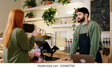 In the modern coffee shop with a perfect atmosphere charismatic barista guy using the smartphone to take a online order from the customer and type on the laptop while on the background Afro American - Powered by Shutterstock