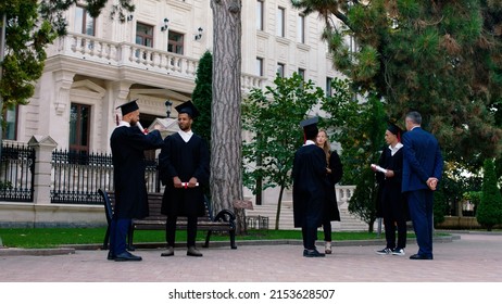 In The Modern College Park In The Graduation Day Group Of Multiracial Students Waiting To Make Some Pictures They By The Way Discussing With College Principal Wearing Graduation Suits And Caps