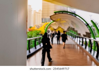 A modern, colorful pedestrian bridge with a curving canopy. People are walking along the wooden pathway, with vibrant colors and city buildings in the blur background. - Powered by Shutterstock