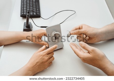 Modern compact hearing aids. Small hearing aids in hands. Closeup of patient and doctor. Hearing rehabilitation clinic selecting digital device for deaf people.