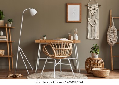 Modern composition at boho interior of home office room with wooden desk, stylish armchair, bamboo shelf, carpet, macrame, mock up poster frame, office supplies, decoration and personal accessories. 