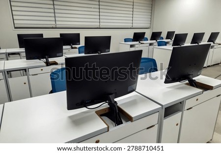 Modern computer classroom with rows of monitors and white desks