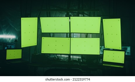 Modern computers with green screens placed on desk in dark room with shimmering lamps on illegal hacker base at night - Powered by Shutterstock