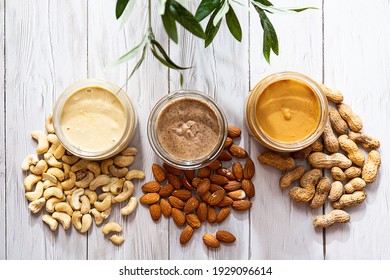 Modern concept of wellness and veganism. Jars of almond, cashew and peanut butter on a white wooden table with an olive branch. Organic, homemade nut butter for a healthy breakfast.