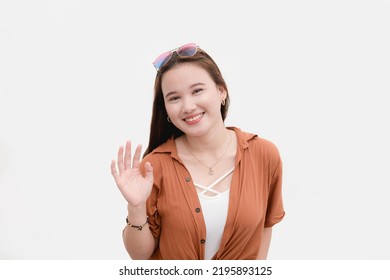 A Modern Congenial Young Asian Woman Saying Hi. Waving Her Hand. Isolated On White Backdrop.