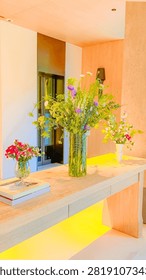 A modern console table made of light wood features three glass vases filled with fresh colorful wildflowers in a bright contemporary interior space.