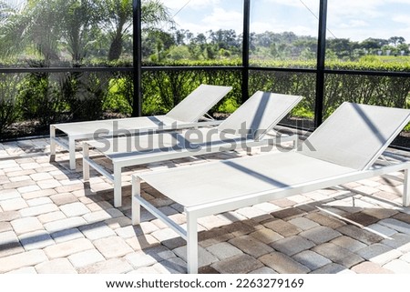 Modern contemporary home villa with screened in glass lanai private pool with deck chairs in Florida and nobody with tropical palm trees plants