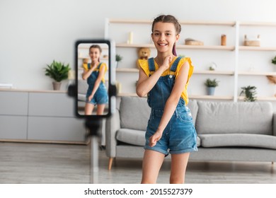 Modern Content Creator Concept. Portrait of positive teenage girl filming her dancing tutorial video for social network, using cellphone on tripod in living room, selective focus - Powered by Shutterstock