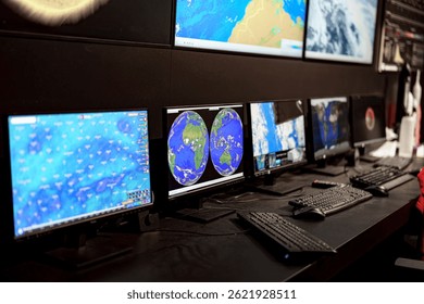 A modern control room filled with multiple computer screens displaying weather maps and satellite images. Professionals are analyzing data for research and forecasting.