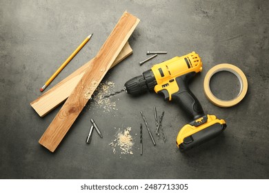 Modern cordless electric drill, sawdust, planks and bits on grey table, flat lay