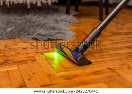 modern cordless vacuum cleaner. The motorised fluffy head reveals all the dust on the laminate floor with a green light. New cyclone technologies modern home cleaning. House cleaning concept.