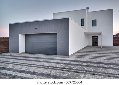 Modern Country House With Gray-white Facade On The Sky Background. Around The House There Is A Tiled Area And A Wooden Fence. Outside. Horizontal.