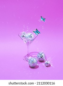 A modern creative idea for a drink with disco balls with glow and blue butterflies on a purple background. The concept of retro fashion aesthetic entertainment of the 80s or 90s.