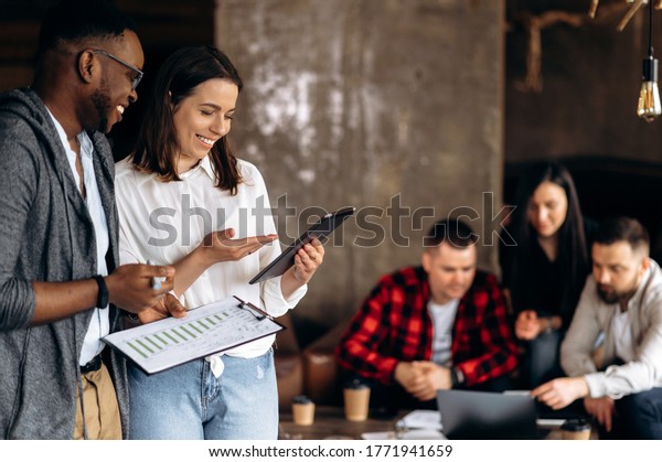 Modern creative\
office.  Successful colleagues are divided into groups to develop\
new ideas. African-American guy and a Caucasian girl look at a\
tablet and discuss new\
startup