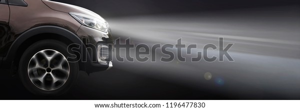 modern crossover car shines with headlights on a\
dark background. side\
view
