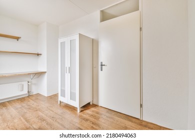 Modern cupboard and vintage chest placed near doors and wicker basket in spacious room with white walls and wooden floor