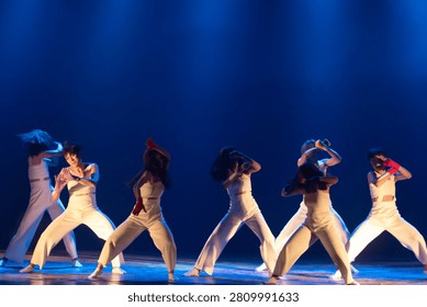 Modern dance ensemble captured in coordinated choreography with expressive movement under vivid blue theatrical lighting.