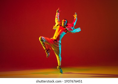 Modern dance. Hip-hop male dancer athletic man dancing in stylish white attire isolated over colorful background in red neon light. Youth culture, fashion, action, freestyle. Copy space for ad