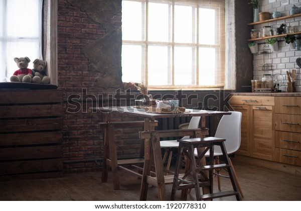 Modern dark loft style kitchen, large window and\
bricks on the walls. A large table in the middle of the kitchen of\
the house. Rustic.
