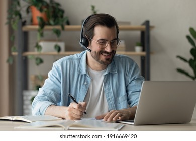 Modern day student. Confident young man in earphones watch virtual lecture lesson on laptop screen take some notes. Millennial male training professional skills get knowledge on webinar online course