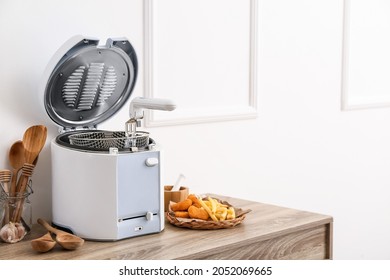 Modern Deep Fryer, French Fries, Nuggets And Kitchen Utensils On Table Near Light Wall