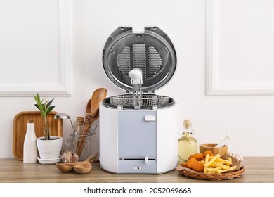 Modern Deep Fryer, French Fries, Nuggets And Kitchen Utensils On Table Near Light Wall