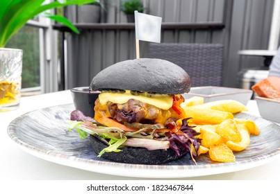 Modern Delicious Black Burger With Meat, Bun, Lettuce, Cheese, Ketchup, French Fries. Funk Food Concept