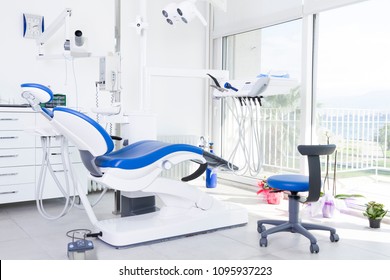 Modern Dental Clinic, Dentist Chair And Other Accessories Used By Dentists In Blue Medical Light. Dental Surgeon, Is A Surgeon Who Specializes In Dentistry And Treatment Of Conditions Of Oral Cavity.