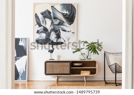 Modern design home interior of living room with wooden commode, design black armchair, tropical leafs and elegant accessories. Stylish home decor. Mock up abstract paintings on the wall. Template.