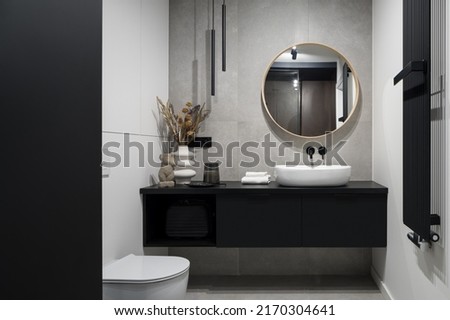 Modern designed bathroom with decorative concrete wall, round mirror over washbasin in black cabinet and toilet
