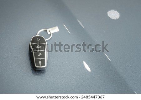 A modern designed car key which is placed on metallic car hood. Object of transportation vehicle, close-up and selective focus. 