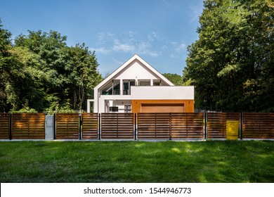 Modern Designed House With Garage And Stylish Wooden Fence Surrounded By Trees