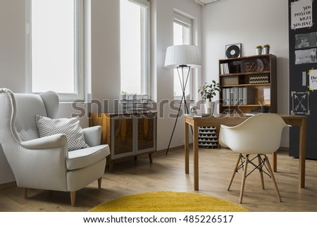 Modern designed room interior with an armchair with cushions, yellow carpet, wooden case, commode, desk and minimalistic chair