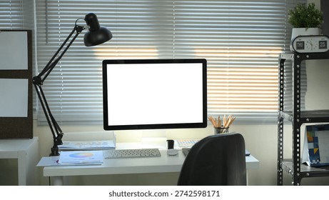 Modern designer workspace with blank computer screen, desk lamp, color charts, and stationery in a creative office.